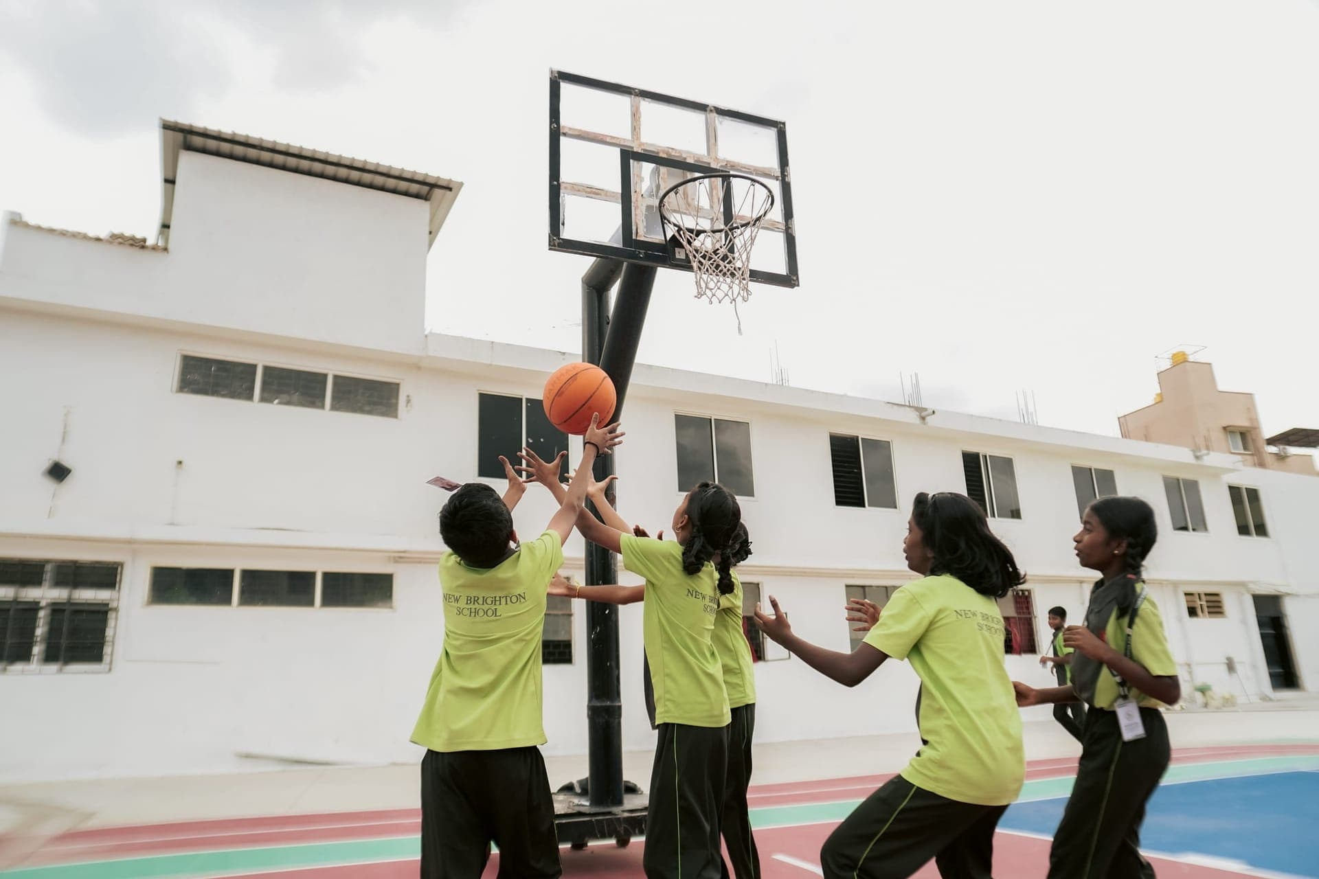Students reaching for the ball under the basketball hoop on the school court